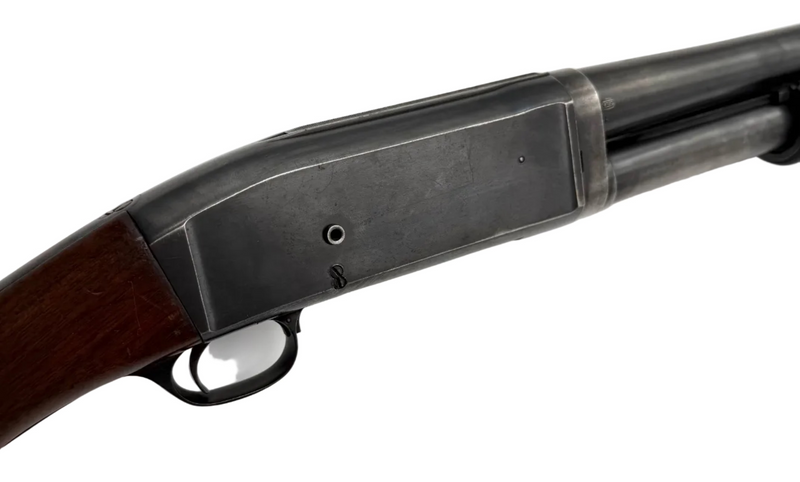 Remington Model 10 12 gauge pump-action shotgun with wooden stock and metal barrel, shown from the side.